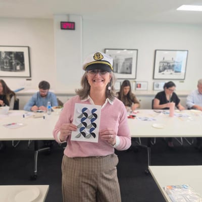 Woman wearing captain hat holding artwork in classroom